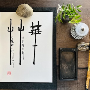 May include: A white sheet of paper with black calligraphy on it. The calligraphy is in Japanese and reads "山  禅". There is a small red stamp in the bottom left corner of the paper. The paper is on a black mat.