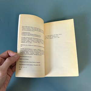 May include: An open book with text on the pages. The left page details publication and copyright information. The right page contains a dedication. The book is held open by a hand, against a blue background.