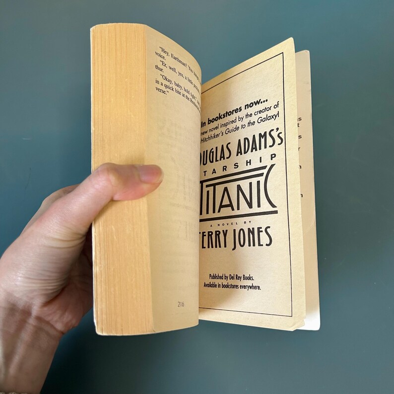 May include: A paperback book titled "Titanic" by Terry Jones, held open to reveal text. The cover features the author's name and the title in a bold, stylized font. The book is open to page 216.