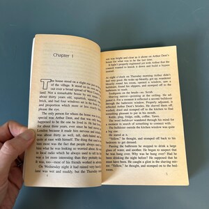 May include: An open book with text on aged pages. The text is divided into chapters, with the first chapter titled "Chapter 1". The text describes a house and the events of a Thursday morning.