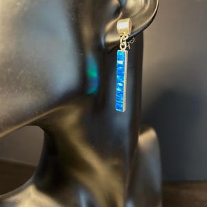 Puede incluir: Un par de pendientes de plata con una piedra de ópalo azul. Los pendientes son largos y rectangulares.