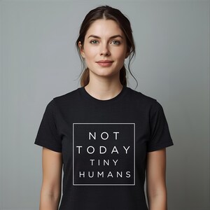 May include: Black t-shirt with the text "NOT TODAY TINY HUMANS" in a white square. The shirt is short-sleeved and the text is in a bold, sans-serif font. The person in the image is wearing the shirt.