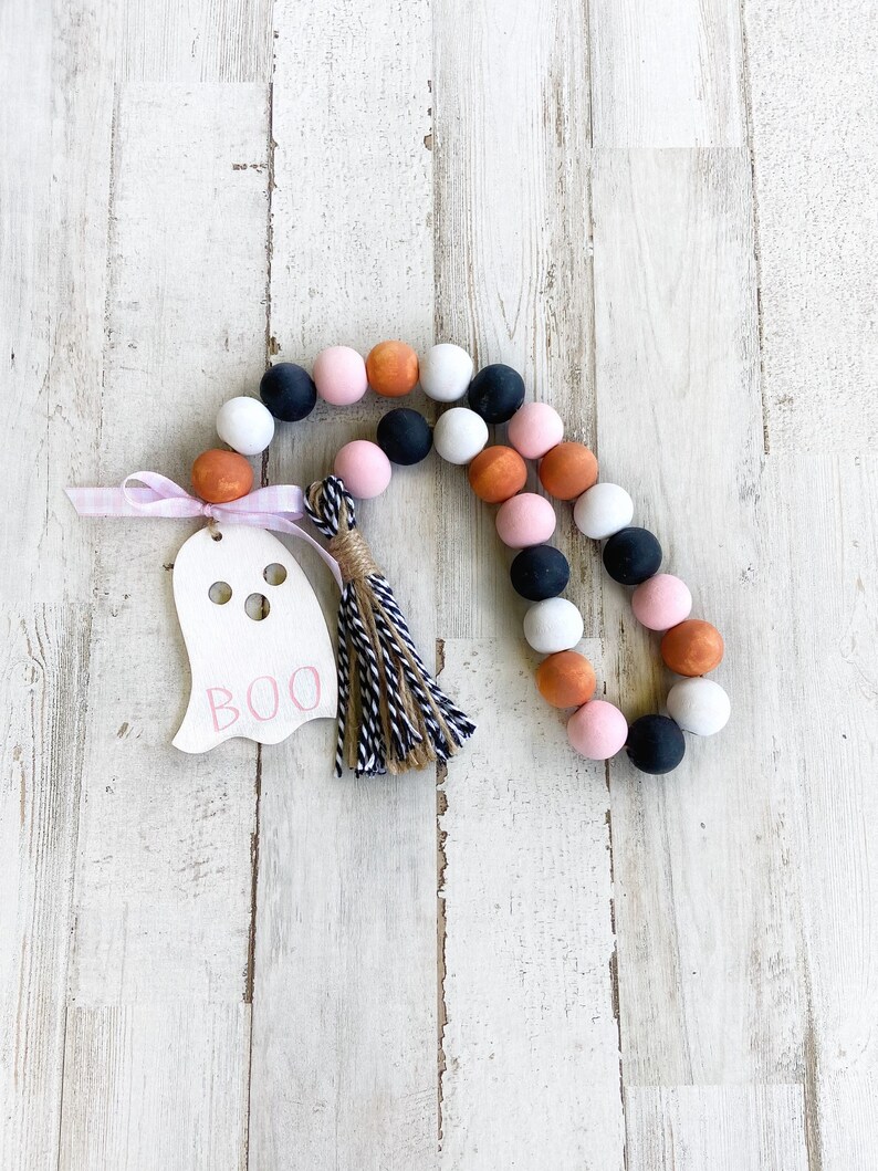 May include: A Halloween-themed beaded garland with black, white, pink, and orange beads. A wooden ghost cutout with the word "BOO" is attached to the garland.
