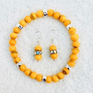 May include: A stretch bracelet and a pair of matching drop earrings featuring round yellow beads with brown wood-grain patterns. The jewelry set includes silver-toned metal spacers and small silver-toned rings embedded with tiny clear crystals.