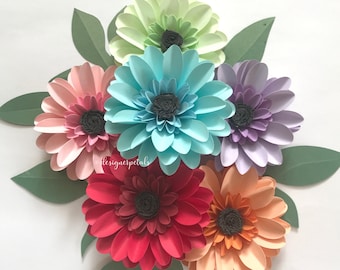 May include: A collection of six handcrafted paper flowers in shades of light green, turquoise, lavender, pink, red, and peach, each featuring a dark gray textured center and surrounded by several matte green paper leaves with the text designerpetals.