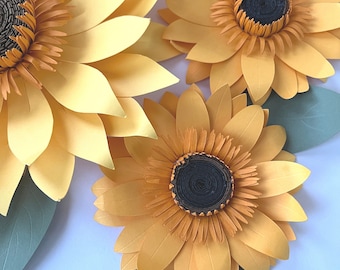 May include: Three large paper sunflowers with yellow petals and brown centers. The sunflowers are arranged in a cluster with green leaves.
