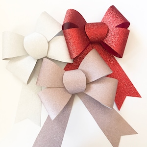 May include: Three large glittery bows in white, silver, and red. The bows are made of paper and have a shiny finish.