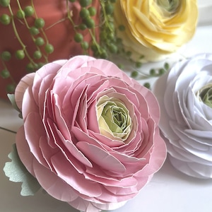 Könnte beinhalten: Nahaufnahme von drei Papierblumen in Rosa-, Weiß- und Gelbtönen. Die rosa Blume befindet sich im Vordergrund, mit einem hellgrünen und gelben Zentrum. Die weiße Blume befindet sich rechts, und die gelbe Blume im Hintergrund. Grün ist sichtbar.