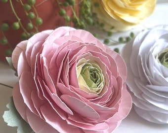 Könnte beinhalten: Nahaufnahme von drei Papierblumen in Rosa-, Weiß- und Gelbtönen. Die rosa Blume befindet sich im Vordergrund, mit einem hellgrünen und gelben Zentrum. Die weiße Blume befindet sich rechts, und die gelbe Blume im Hintergrund. Grün ist sichtbar.