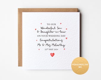 May include: A white card with a brown envelope. The card has red hearts and black text that reads "To our wonderful son & daughter-in-law on your wedding day. Congratulations Mr & Mrs McCarthy 22nd May 2024".