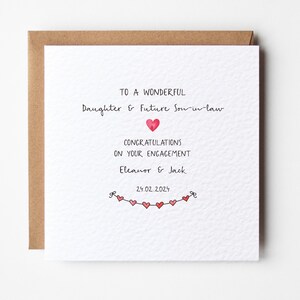 Puede incluir: Una tarjeta blanca con un sobre marr&oacute;n. La tarjeta tiene un mensaje escrito a mano que dice "To a wonderful Daughter & Future Son-in-law Congratulations on your engagement Eleanor & Jack 29.02.2024". Hay peque&ntilde;os corazones rojos dibujados en la parte inferior de la tarjeta.