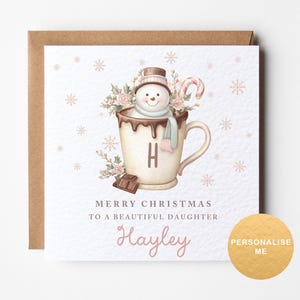 May include: A Christmas card design with a snowman in a hot chocolate mug, decorated with a candy cane and flowers. The card includes the text "Merry Christmas to a Beautiful Daughter" and a personalized name. The background is white with snowflake details.
