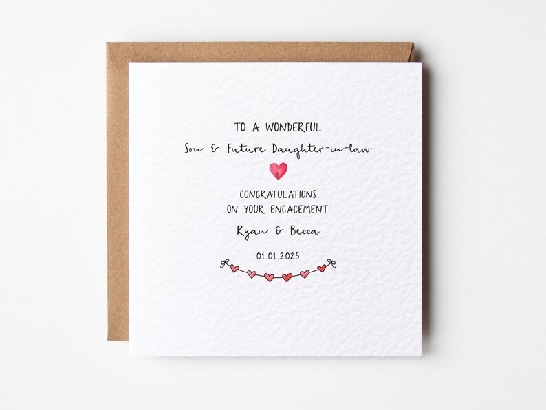 May include: A white card with a brown envelope. The card has a handwritten message that says "To a wonderful Son & Future Daughter-in-law Congratulations on your engagement Ryan & Becca 01.01.2025". There is a string of red hearts at the bottom of the card.