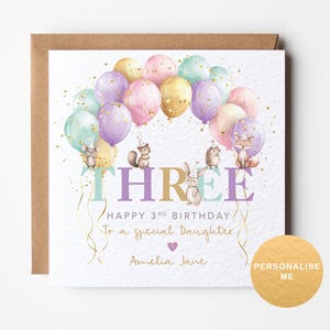 May include: A white card with a pink, purple, and gold balloon design. The card says "Happy 3rd Birthday to a special daughter, Amelia Jane".