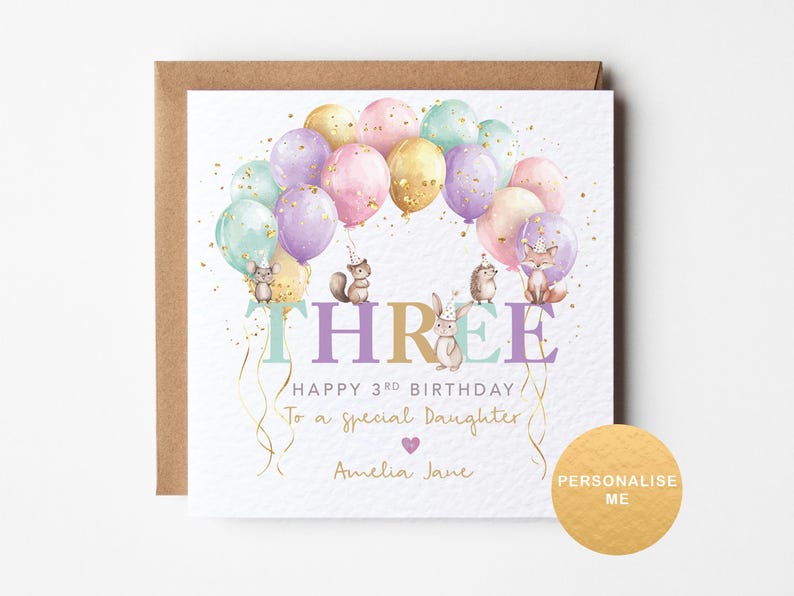 May include: A white card with a pink, purple, and gold balloon design. The card says "Happy 3rd Birthday to a special daughter, Amelia Jane".