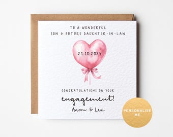 May include: A white card with a pink heart balloon illustration and the text "To a wonderful son & future daughter-in-law 21.10.2024 Congratulations on your engagement! Aaron & Lexi".