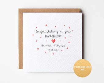 May include: A white card with a red heart design and the text "Congratulations on your ENGAGEMENT Hannah & Joshua 18.11.2023".