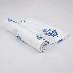 Puede incluir: Tela de algod&oacute;n blanca con estampado floral azul. La tela est&aacute; enrollada y el estampado floral es visible en la parte superior e inferior del rollo.