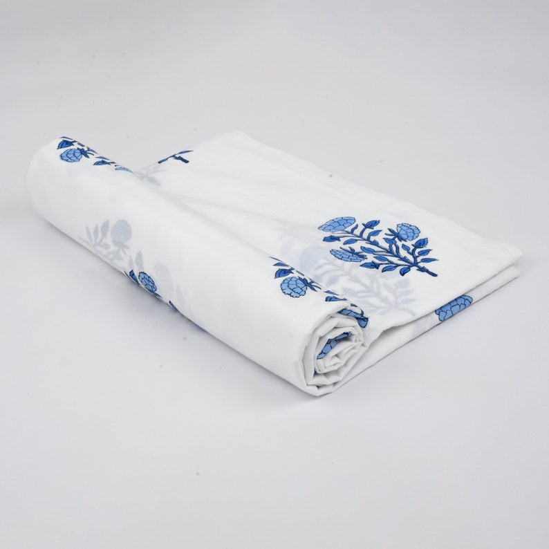 Puede incluir: Tela de algod&oacute;n blanca con estampado floral azul. La tela est&aacute; enrollada y el estampado floral es visible en la parte superior e inferior del rollo.