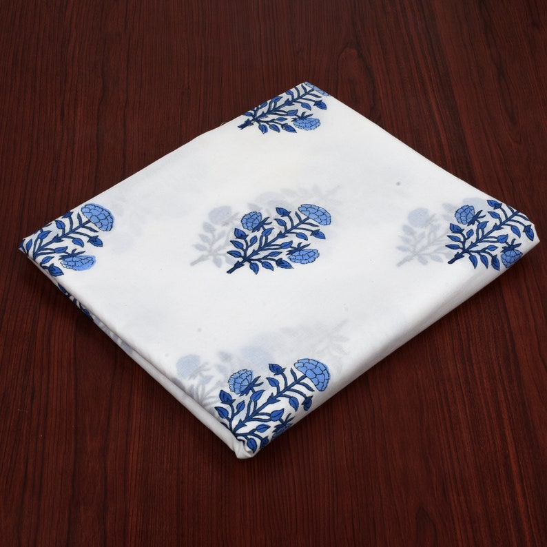 Puede incluir: Tela de algod&oacute;n blanca con estampado floral azul. La tela est&aacute; doblada por la mitad y tiene una textura lisa.