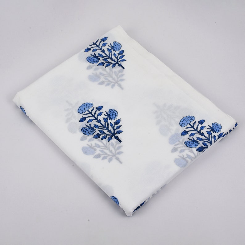 Puede incluir: Tela de algod&oacute;n blanca con estampado floral azul. La tela est&aacute; doblada por la mitad y el estampado floral es visible en ambos lados.