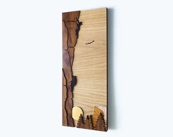 May include: A wooden wall art piece featuring a brown silhouette of a rock climber ascending a cliff face. The background is a light wood grain with a small yellow circle representing the sun. The bottom of the piece features a small forest silhouette.