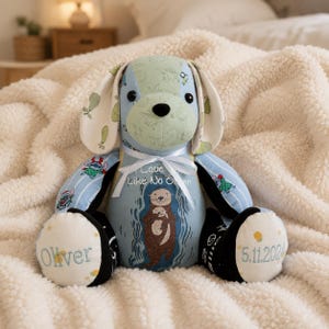 May include: A patchwork dog soft toy in shades of blue and green, with a white ribbon and the text "Love Like No Other". The dog's paws are embroidered with the name "Oliver" and the date "5.11.2024".