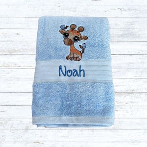 May include: A light blue towel with a brown and orange giraffe with blue birds embroidered on it. The towel has the name "Noah" embroidered below the giraffe.
