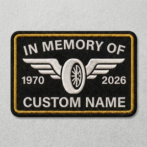 Può includere: Una toppa rettangolare ricamata nera con bordo dorato. Presenta il testo bianco IN MEMORY OF, 1970, 2026 e CUSTOM NAME. Un grafico centrale bianco raffigura uno pneumatico con ali che si estendono da entrambi i lati della ruota.