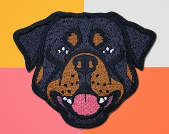 May include: Embroidered patch of a Rottweiler dog's face. The dog has black fur, a brown nose, and a pink tongue sticking out.