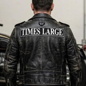 May include: A distressed black leather jacket with the text "TIMES LARGE" in a white rectangle on the back. The jacket has a classic biker style with a notched collar and shoulder epaulets.