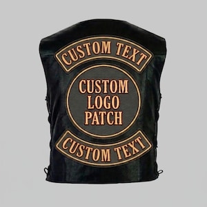 Peut inclure: Gilet en cuir noir avec trois écussons. Les écussons supérieur et inférieur indiquent "CUSTOM TEXT" en couleur or. L'écusson central est circulaire et indique "CUSTOM LOGO PATCH" en or.