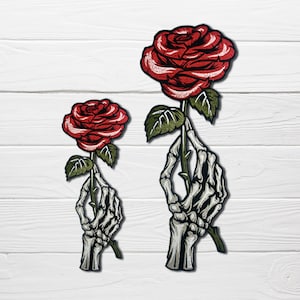 May include: Two embroidered patches featuring a skeleton hand holding a red rose. The larger patch is approximately 5 inches tall and the smaller patch is approximately 3 inches tall.