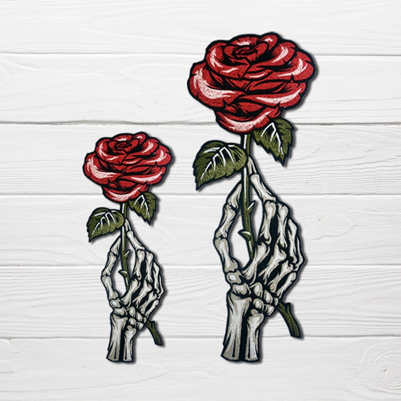 May include: Two embroidered patches featuring a skeleton hand holding a red rose. The larger patch is approximately 5 inches tall and the smaller patch is approximately 3 inches tall.