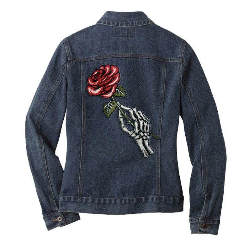 May include: A dark blue denim jacket with a red rose and a skeleton hand holding the stem of the rose embroidered on the back.