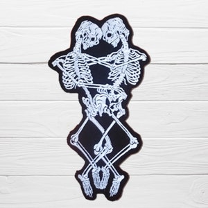 May include: White embroidered skeletons embracing on a black background. The skeletons are intertwined and their hands are clasped together. The patch is perfect for adding a gothic touch to clothing or accessories.