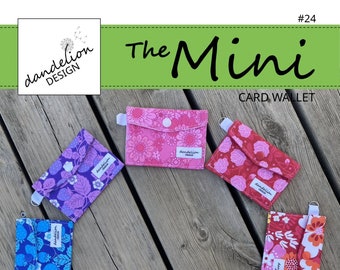May include: Eight colorful mini card wallets with floral patterns. Each wallet has a snap closure and a small loop for attaching a key chain. The wallets are arranged in a circle on a wooden surface. The text "The Mini Card Wallet" is displayed above the wallets.