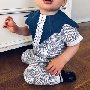 Puede incluir: Un bebé con un mono estampado en blanco y negro con un babero azul y blanco. El babero tiene un borde de encaje.