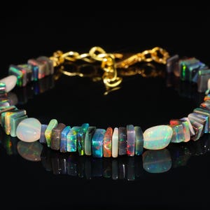 May include: A handmade bracelet with a gold chain and a variety of colourful opal stones. The bracelet includes rectangular and rounded opal beads in shades of blue, green, red, and white. The bracelet is displayed against a black background.