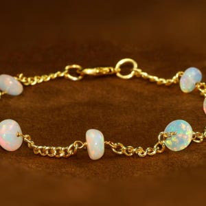 May include: A gold chain bracelet with six white opal beads. The bracelet has a lobster clasp closure.