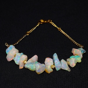 May include: A gold chain bracelet with iridescent opal stones. The opals are irregular in shape, showing white, pink, blue, and yellow hues. The bracelet is set against a black background.