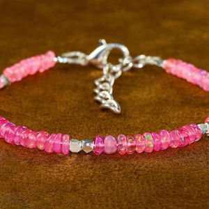 May include: A pink opal bracelet with a silver clasp. The bracelet features small, rounded pink opal beads and silver-coloured metal accents. The clasp has a decorative paw print charm.