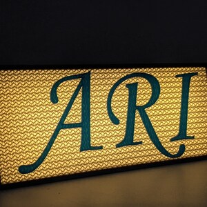 May include: A light-up sign with the word "ARI" in teal lettering on a gold background.