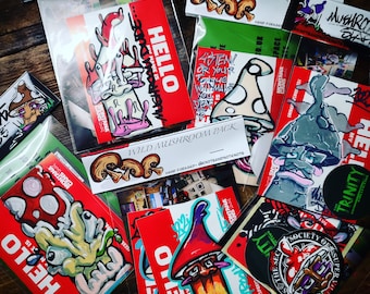 Op de afbeelding: Een verzameling kleurrijke stickers met paddenstoel illustraties en de tekst "Wild Mushroom Pack", "Hello", "Aten! Or Your Tongue Will Make You Deaf", en "The Society of Super Artists".