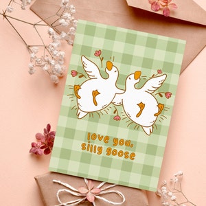 printable silly goose card. soft gingham background with two geese lying on their backs surrounded by flowers. text reads love you silly goose. Printable anniversary card for boyfriend or girlfriend
