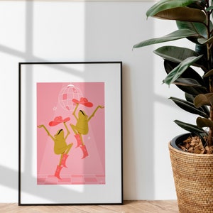 pink dancing frog art print rests against a white wall bathed in sunlight next to a tall house plant. Frogs wear cowboy hat and boots in a sparkling hot pink colour
