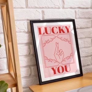 Lucky art print in a black frame in a mid-century home office. Art is pink and red and inspired by retro tarot art. At the bottom of the art, retro red typography reads LUCKY YOU