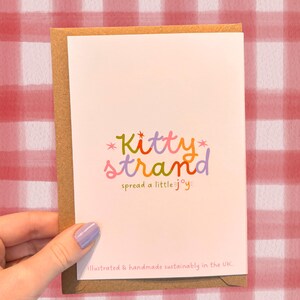 worm Valentine's Day card. pink Valentine's day card with an illustration of two worms surrounded by love hearts and text reading Would I still be your valentine if I were a worm? in red typography. Valentine's Day card for boyfriend, husband or partner held by a woman in front of a cosy background