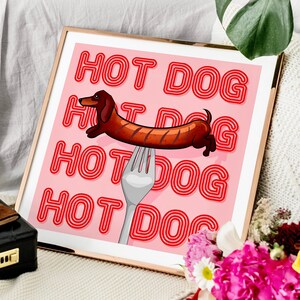 Square, printable pink & red dog art print. Soft pink background with red text in the style of neon lights reading HOT DOG. in the centre of the art print is a dachshund in the shape of a sausage on the end of a silver fork in a playful style