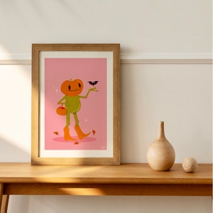 howdy halloween frog art print in pink, green and orange on wooden side. UPS style cartoon illustration of a frog with a pumpkin head wearing orange cowboy boots and carrying a pumpkin bag. next to him flies a little bat, leaves surround his feet